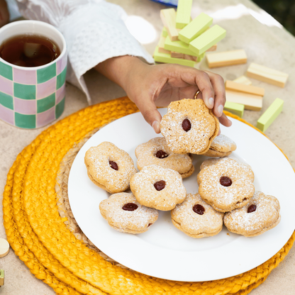 Person picking up a cookie from a plate with a cup of tea and snacks on a table.